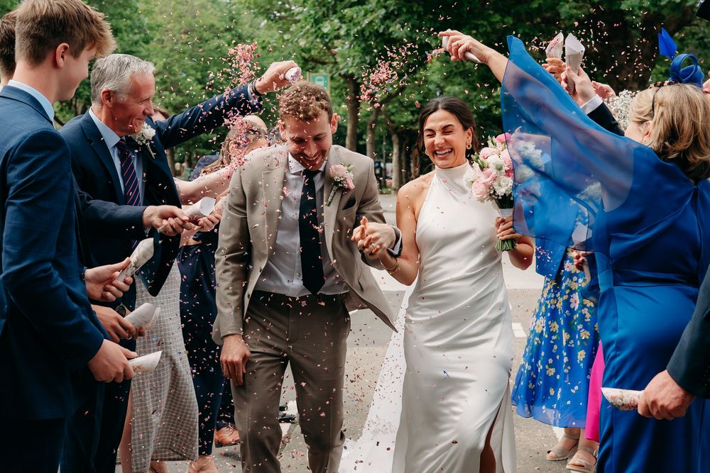 Wedding guests shower the newlyweds with colorful confetti on a sunny outdoor celebration.