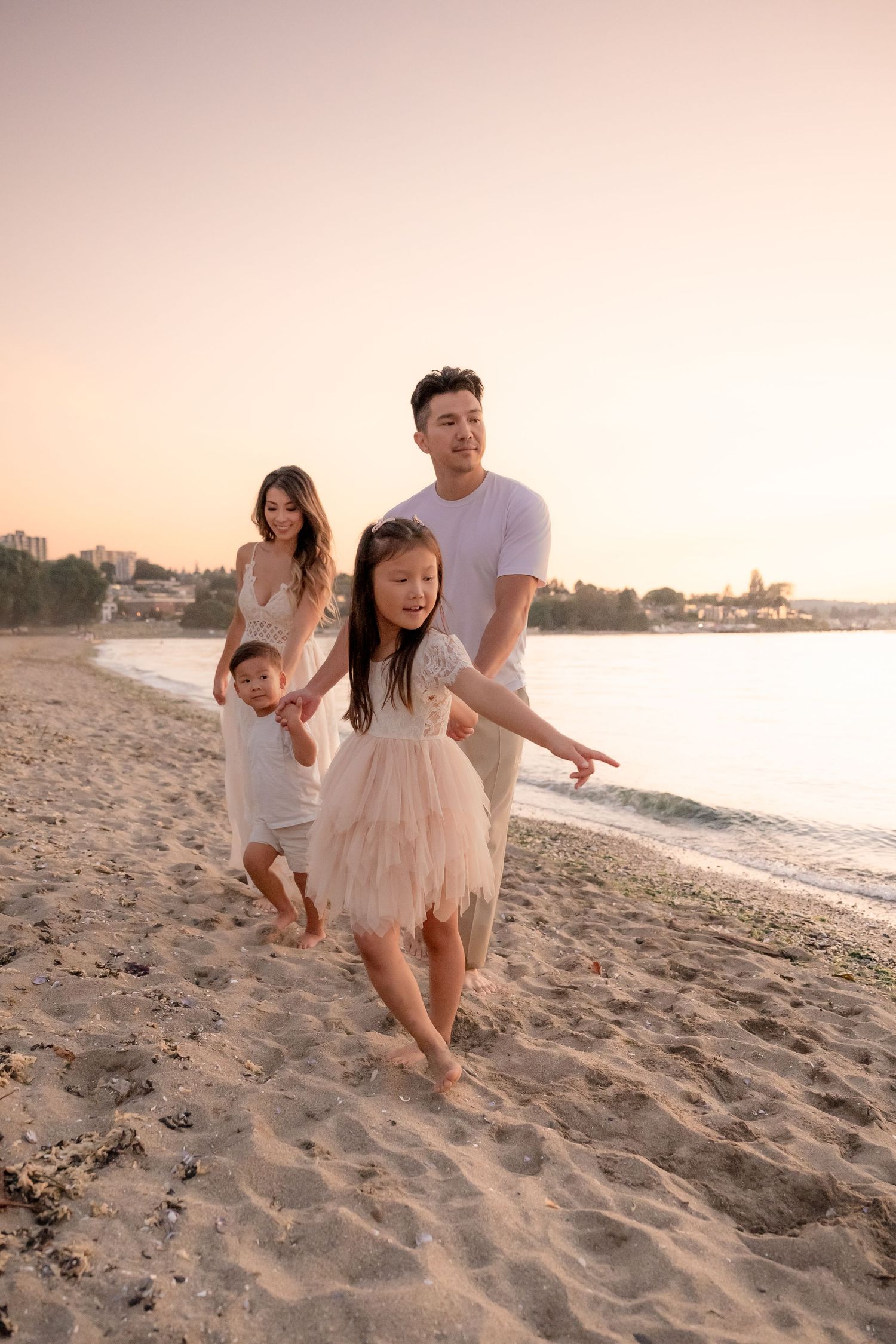Young girl in a white lace dress plays in the sand at sunset on a peaceful beach.