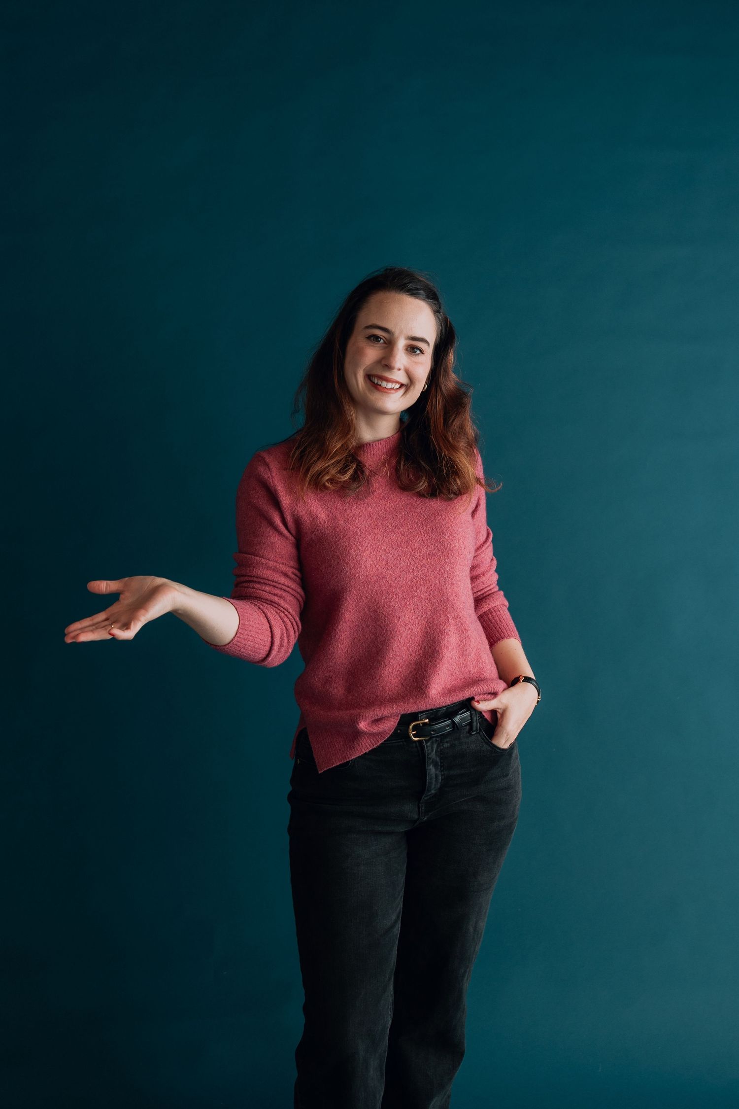 Woman in pink sweater gesturing casually against teal studio backdrop.