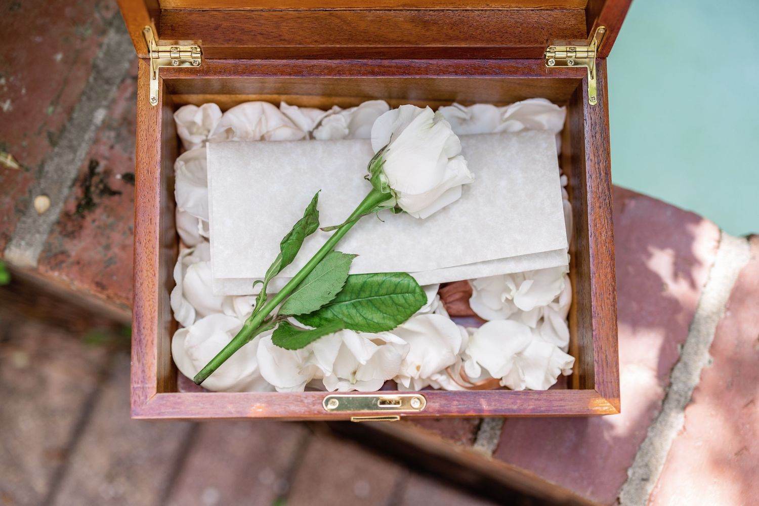 A single white rose with green leaves rests in an elegant wooden box filled with soft fabric padding.