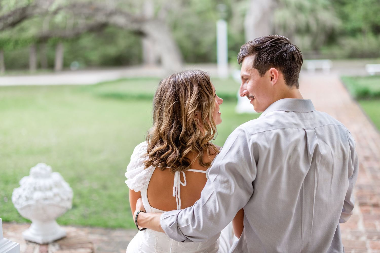 Young couple embrace and gaze at each other in an outdoor garden setting with ornate stone detailing.