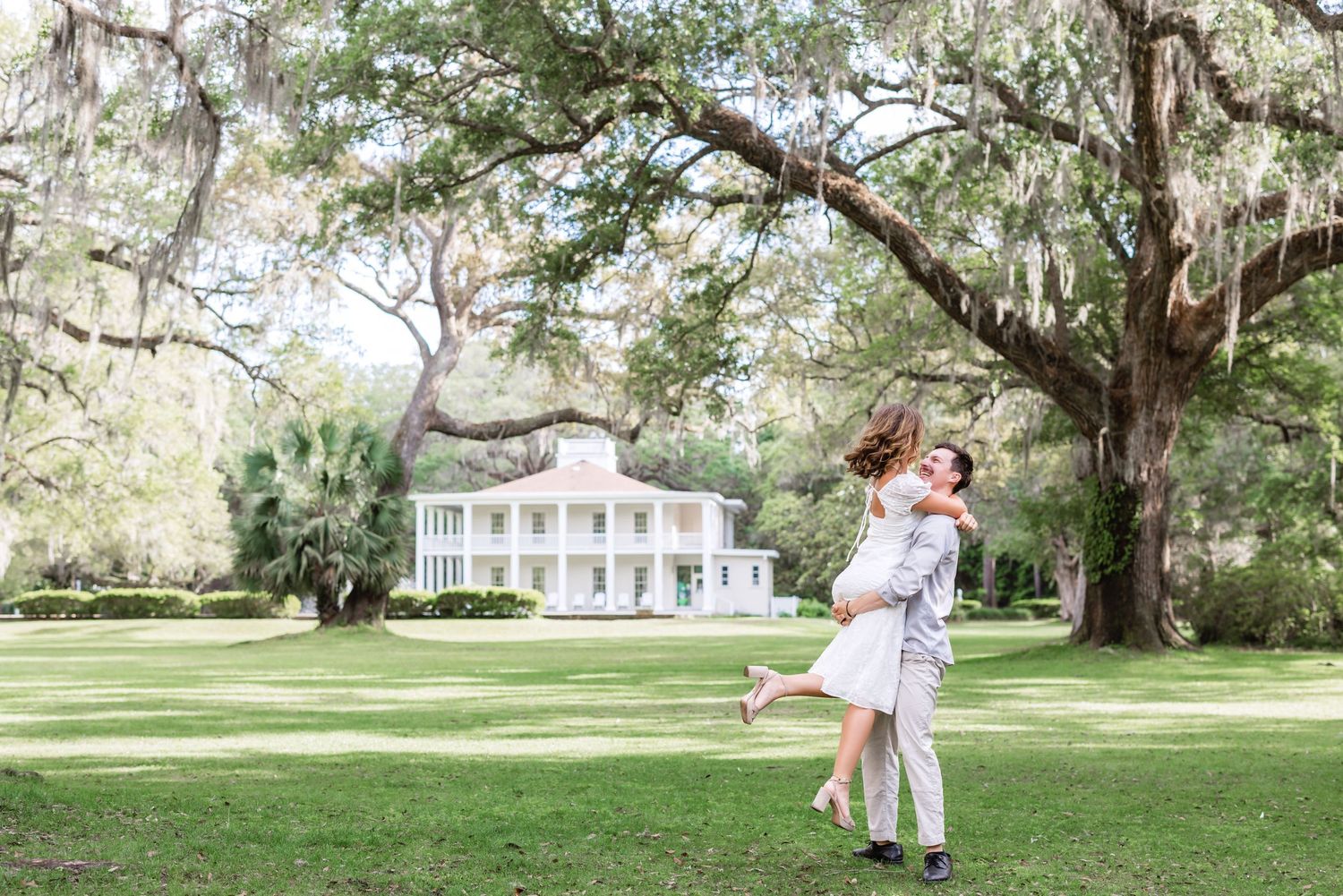 A romantic moment captured in front of a stately Southern plantation home surrounded by Spanish moss-covered oak trees.