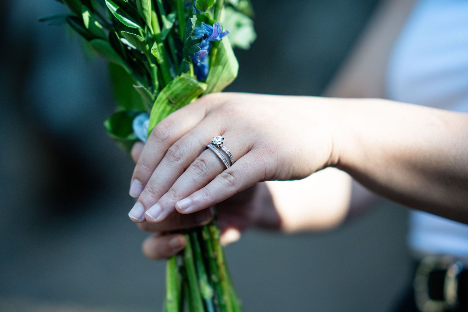Close-up of hands holding a blue flower bouquet with an engagement ring prominently displayed. engagement session colorado springs