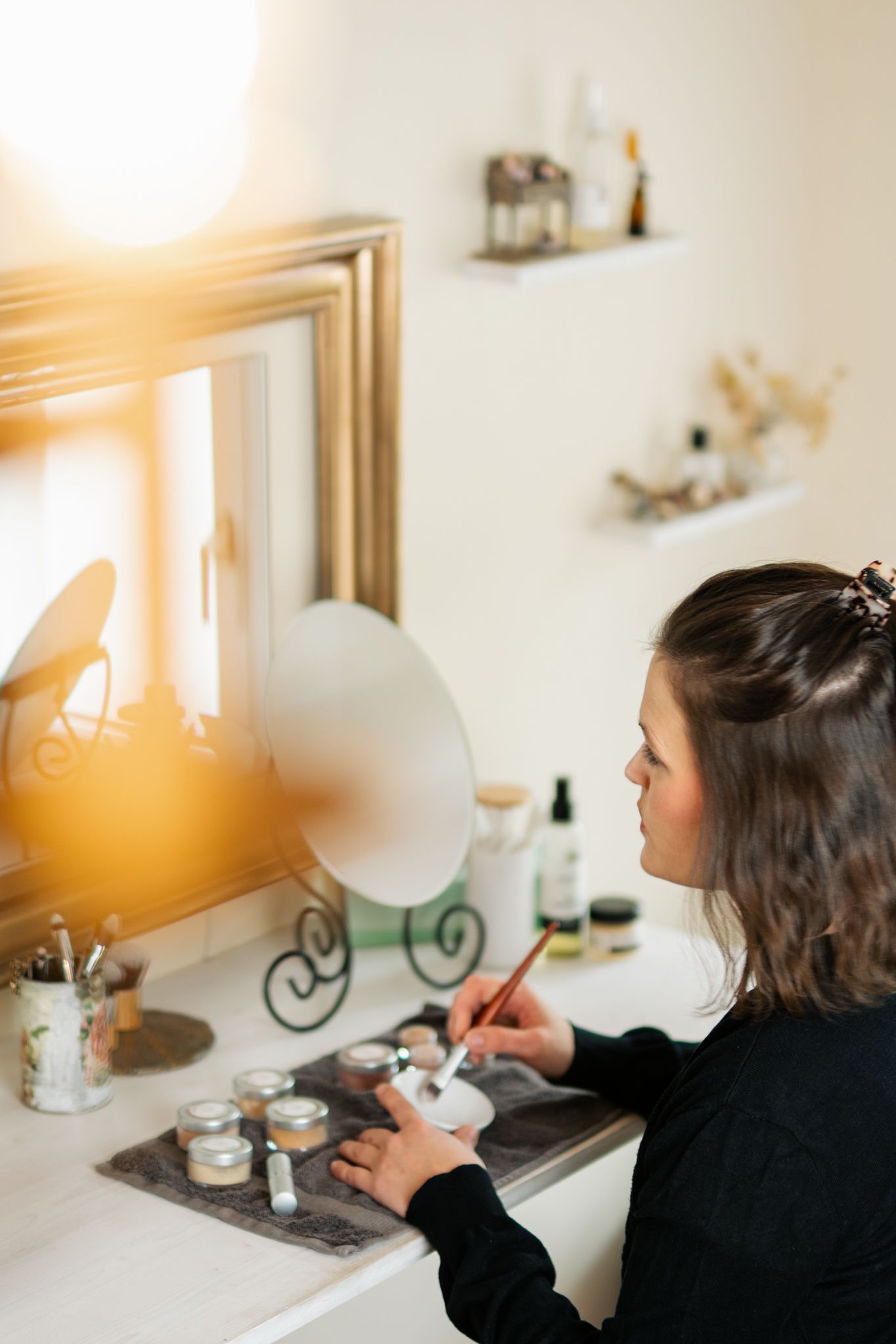 Person working at vanity desk in warm sunlit room with decorative elements.
