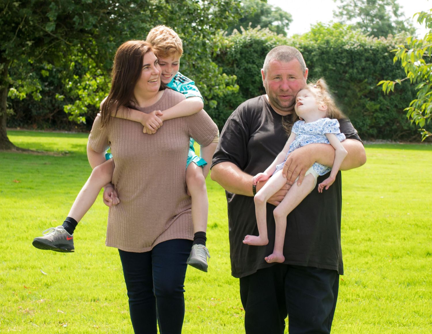 Couple holding a baby outdoors in a green garden setting during a family photo session.