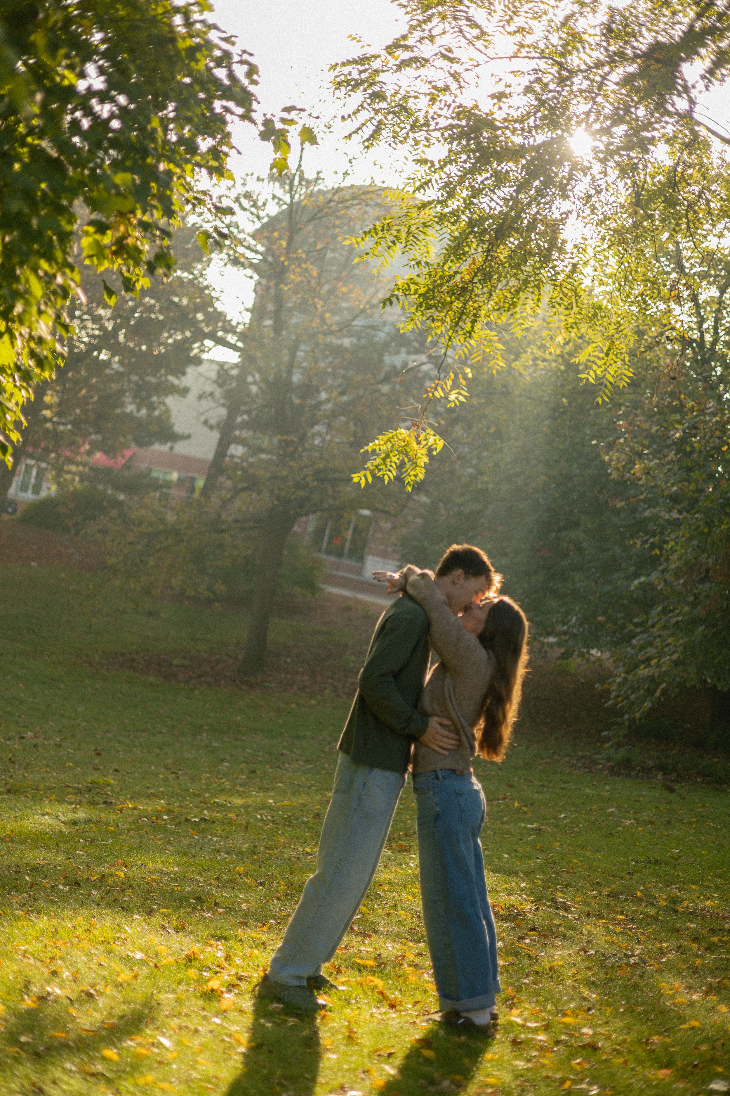 A couple embraces in a sunlit autumn park with golden light filtering through trees in the background.