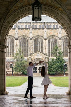A couple plays and spins in a twirl at the Law Quad in University of Michigan in Ann Arbor during their engagement photos.