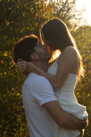 Silhouetted couple embraces in romantic sunset lighting with golden backlight filtering through trees during a golden hour photo session.