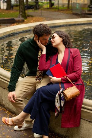 A couple sits intimately by a fountain in a park on an autumn day, sharing tender moments together in Detroit Michigan for couples photos.