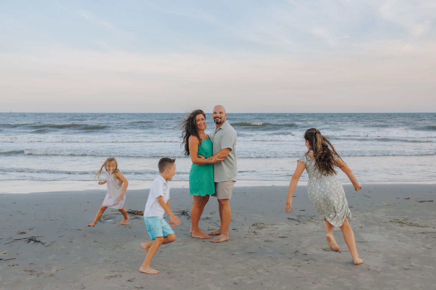 A group portrait of a family holding bouquets of red flowers on a misty beach at sunset.
