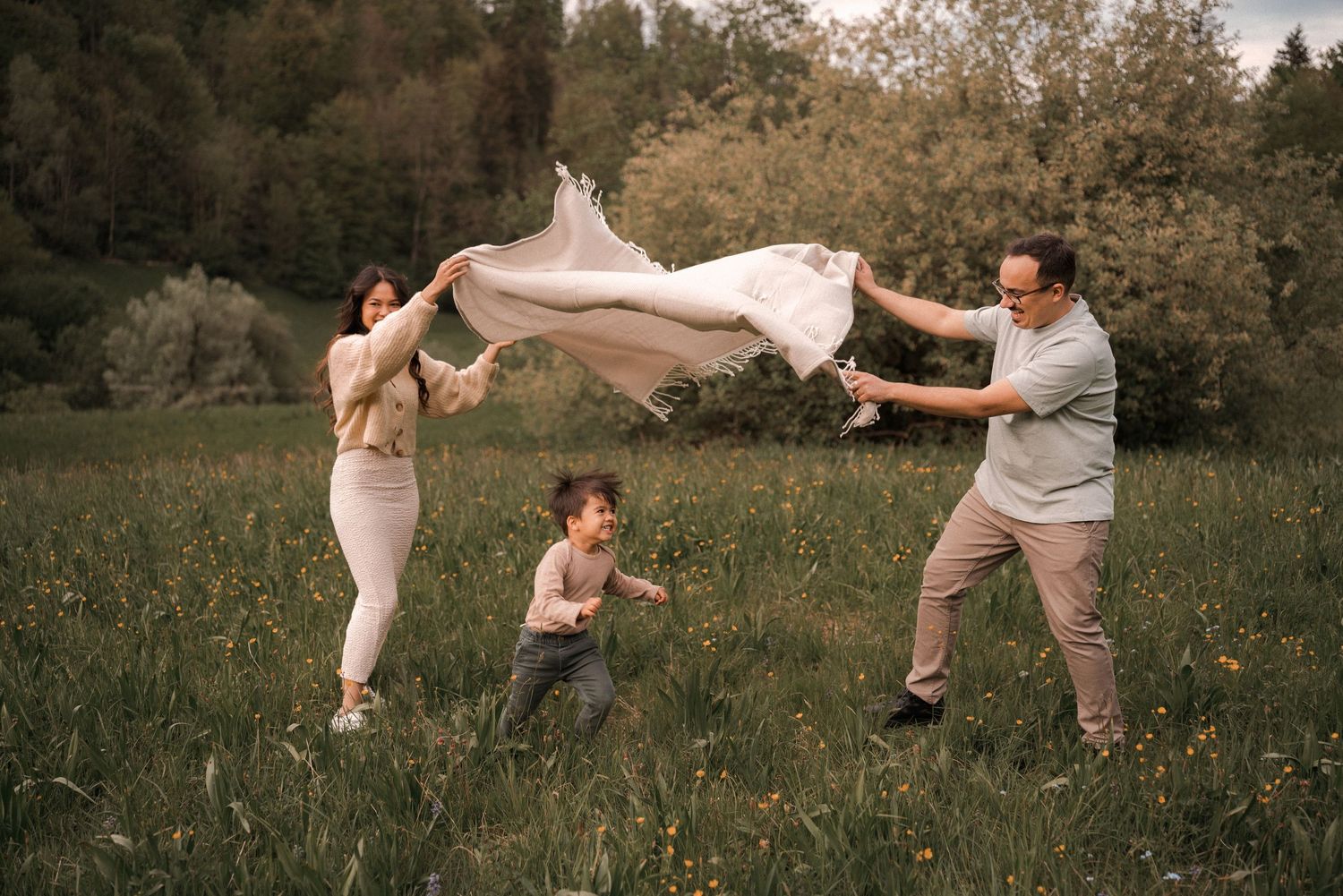A playful family portrait in a meadow with parents swinging their child between them.
