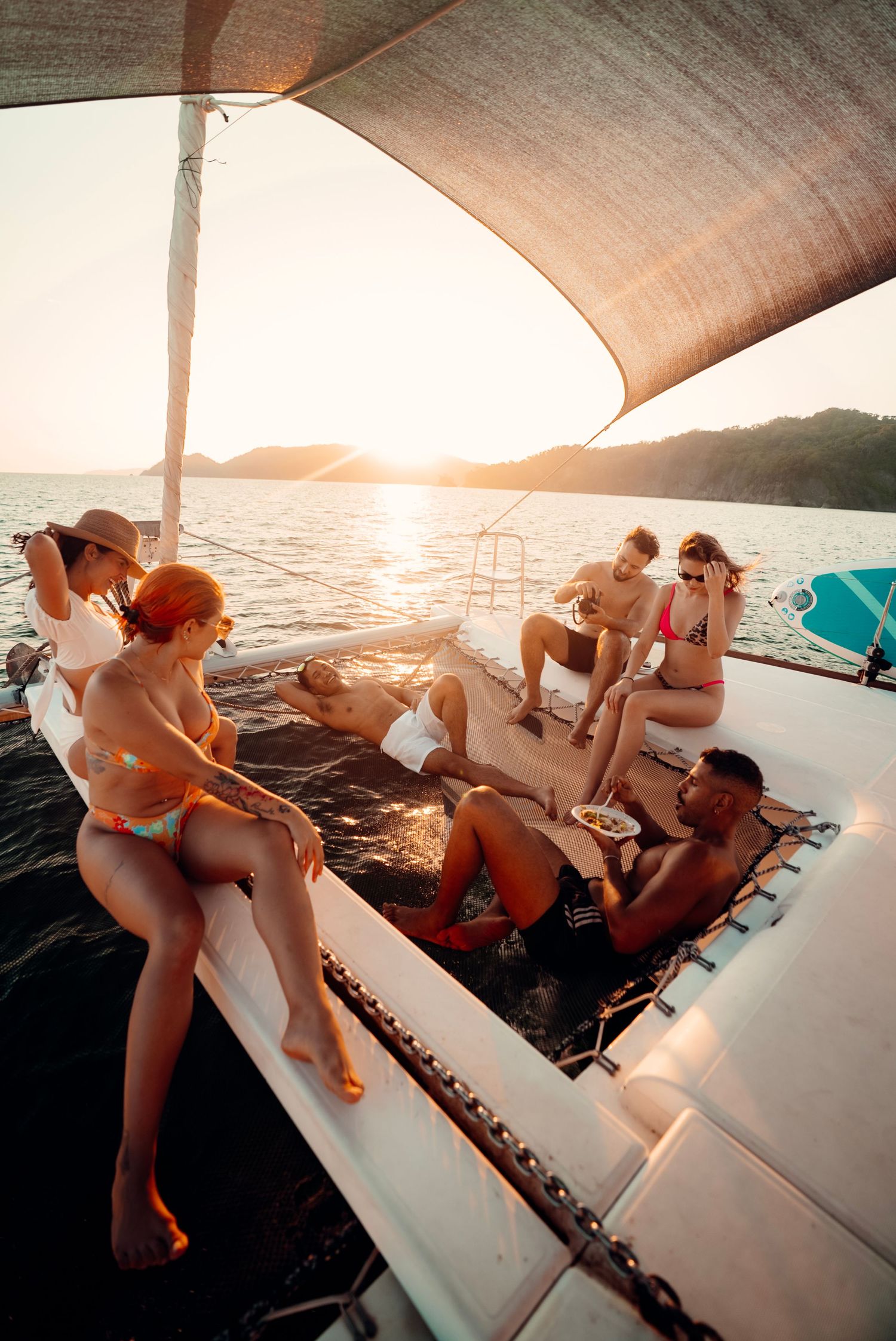 Group of friends lounging on a boat deck at sunset enjoying views of the ocean during a summer cruise.