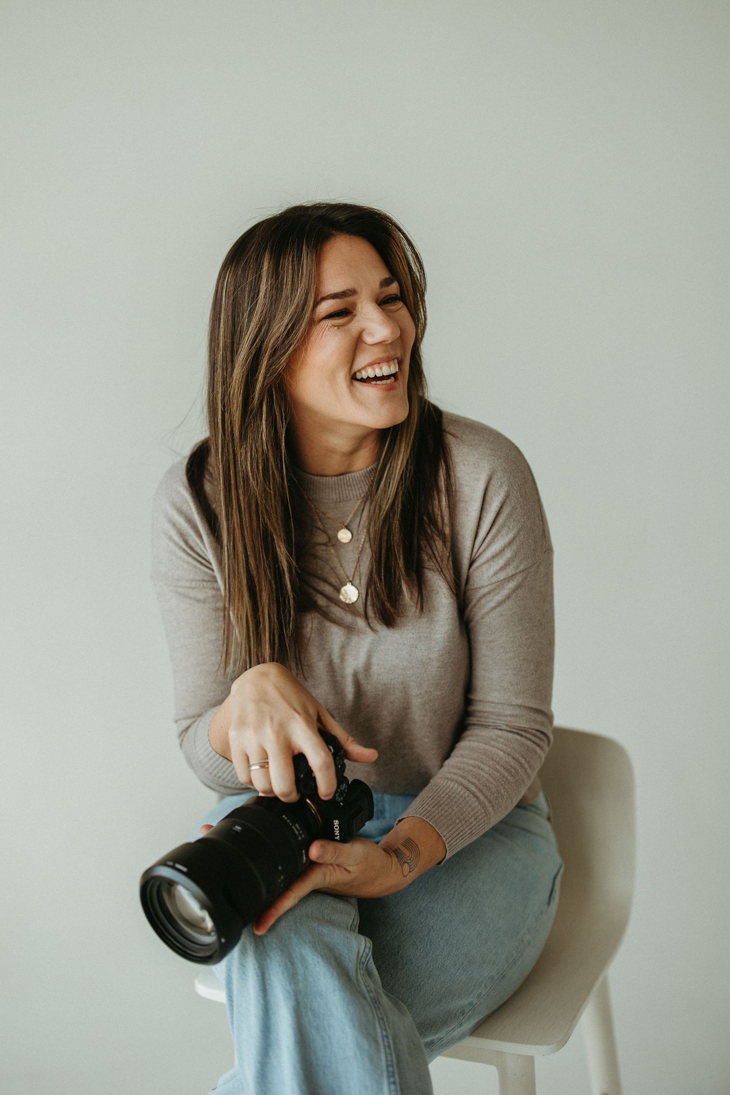 Portrait of photographer holding her camera and smiling in a white studio space.