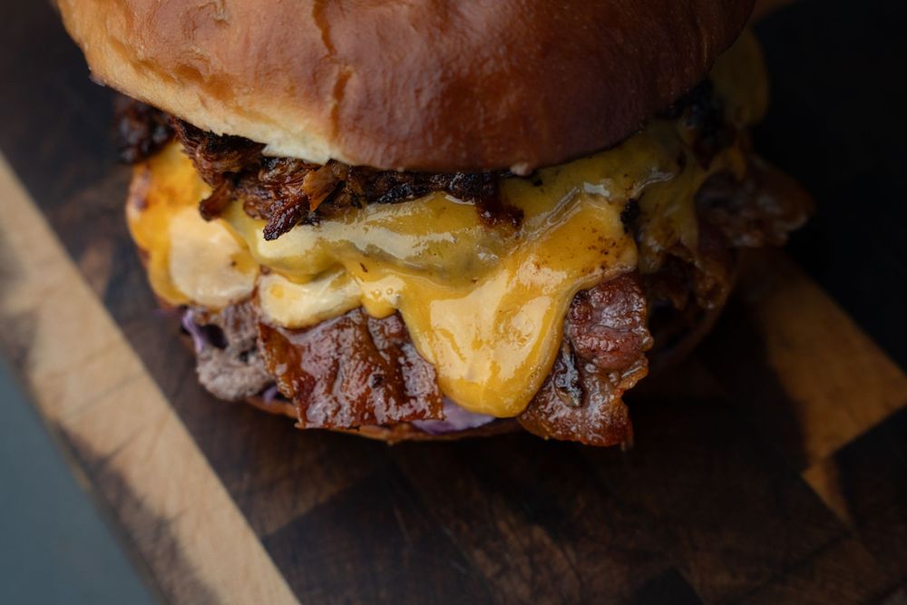 Juicy cheeseburger with melted cheese and toppings shown in multiple stages of assembly on a dark background.