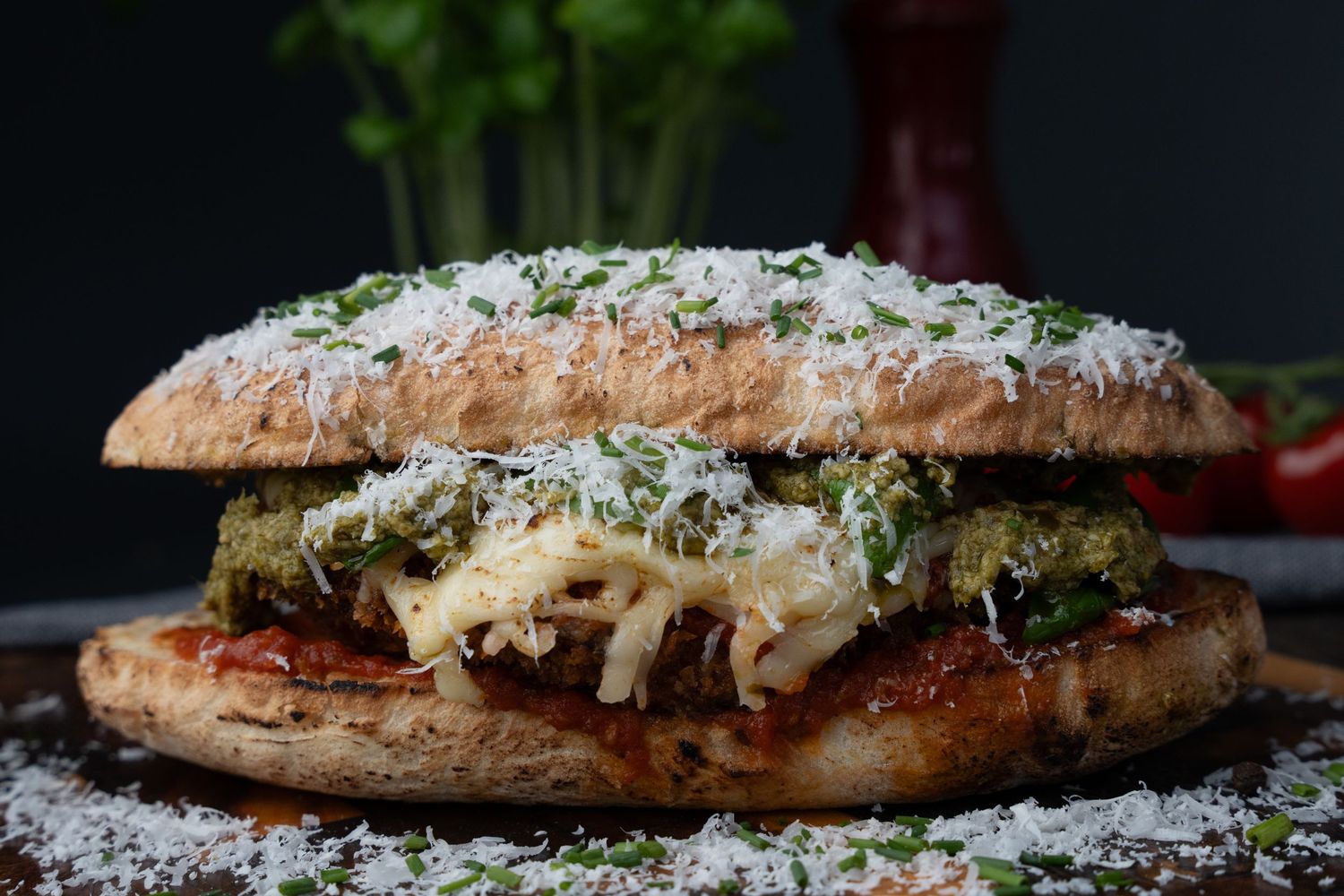 Grilled chicken sandwich topped with melted cheese and fresh herbs on a rustic bread roll.