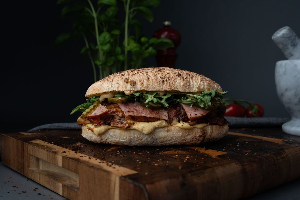 Gourmet burger with caramelized onions and bacon served on a rustic wooden cutting board against dark background.