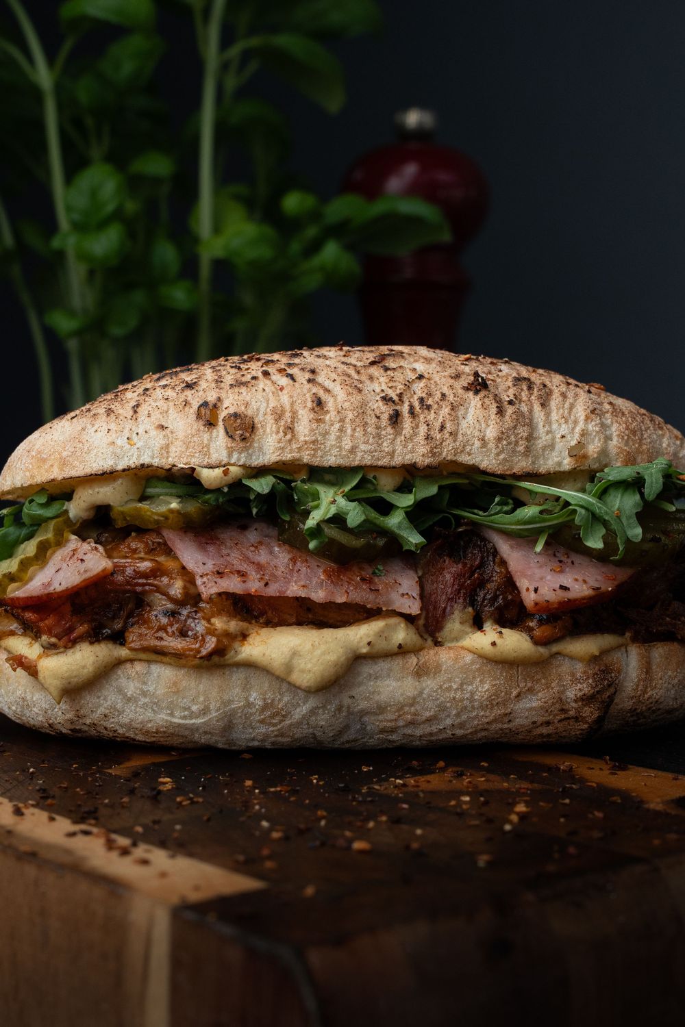 Four rustic artisan sandwiches with meat and fresh greens on wooden boards in dramatic lighting.
