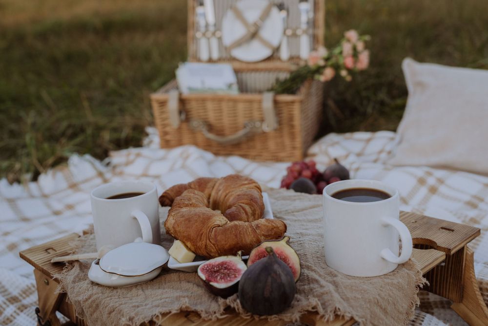 Fresh croissants, figs and coffee cups arranged on wooden board during outdoor picnic.