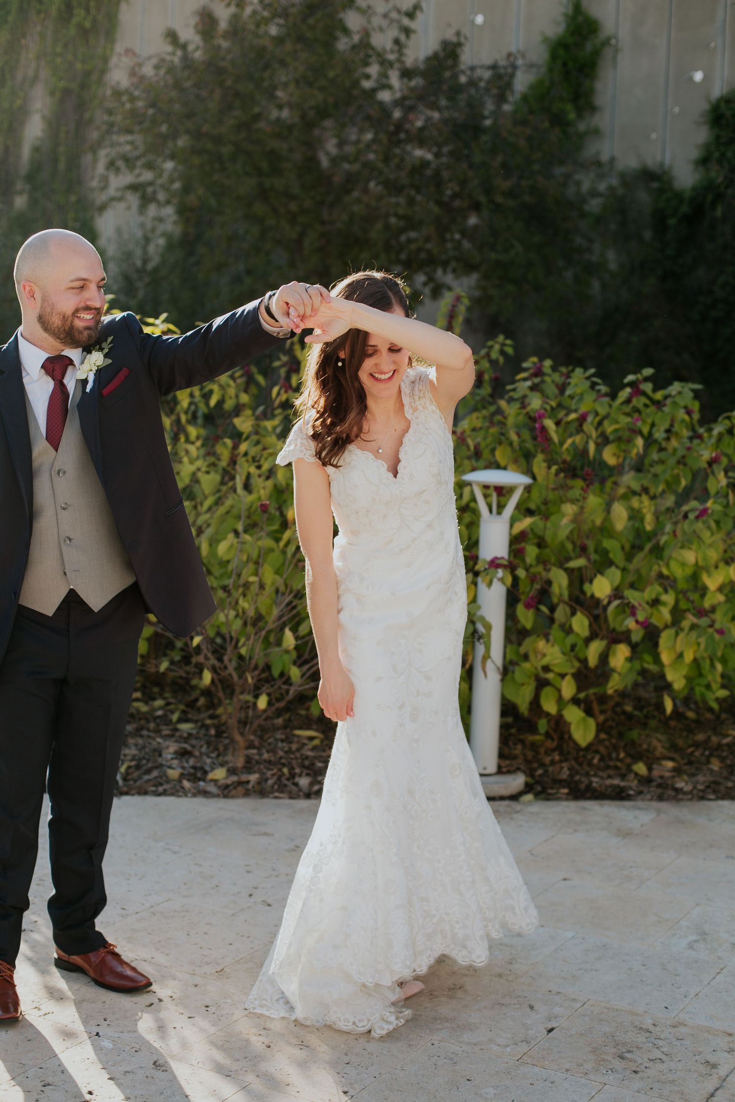 Groom twirls bride in lace wedding dress during outdoor dance.