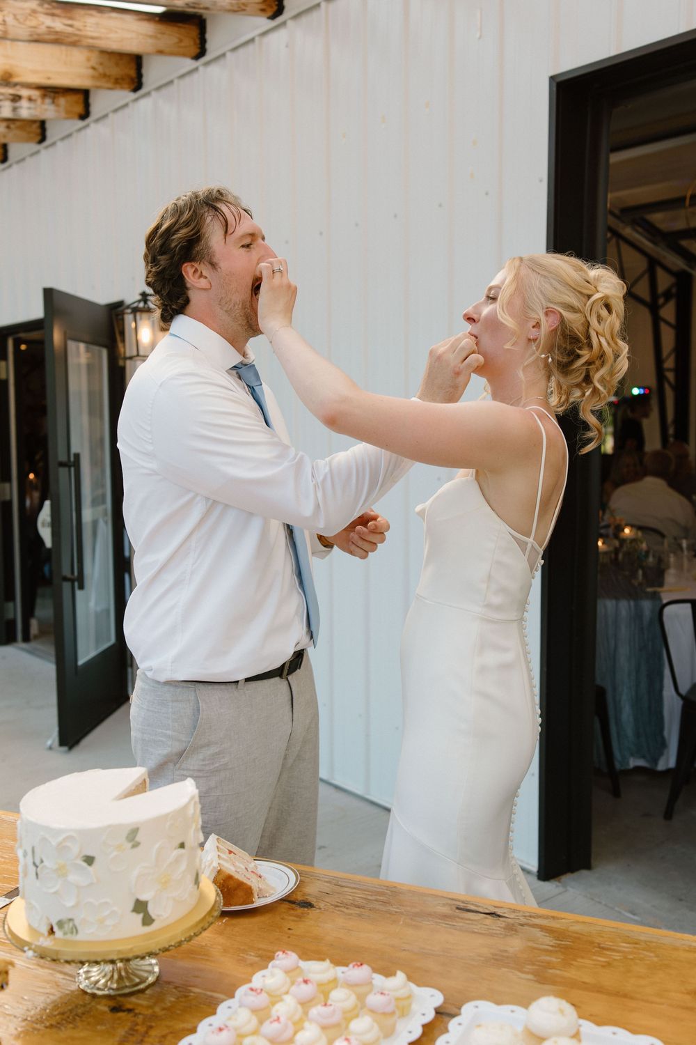 A couple playfully smashing wedding cake on each other's faces during their reception celebration.