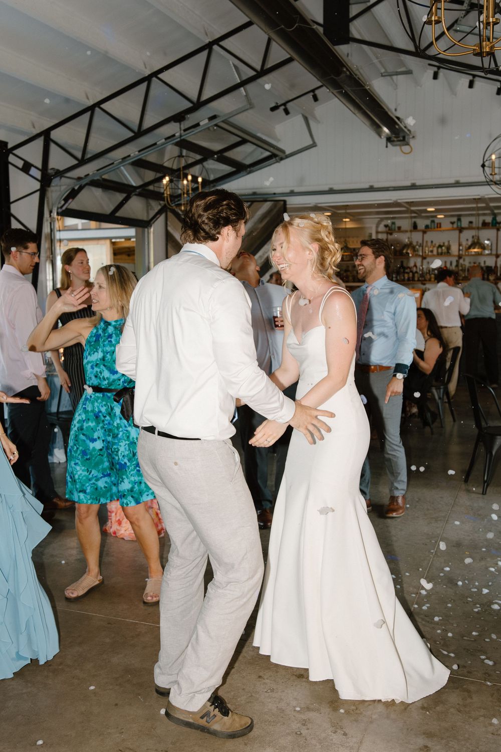 A couple dances together at their wedding reception in an industrial-style venue with exposed beams.
