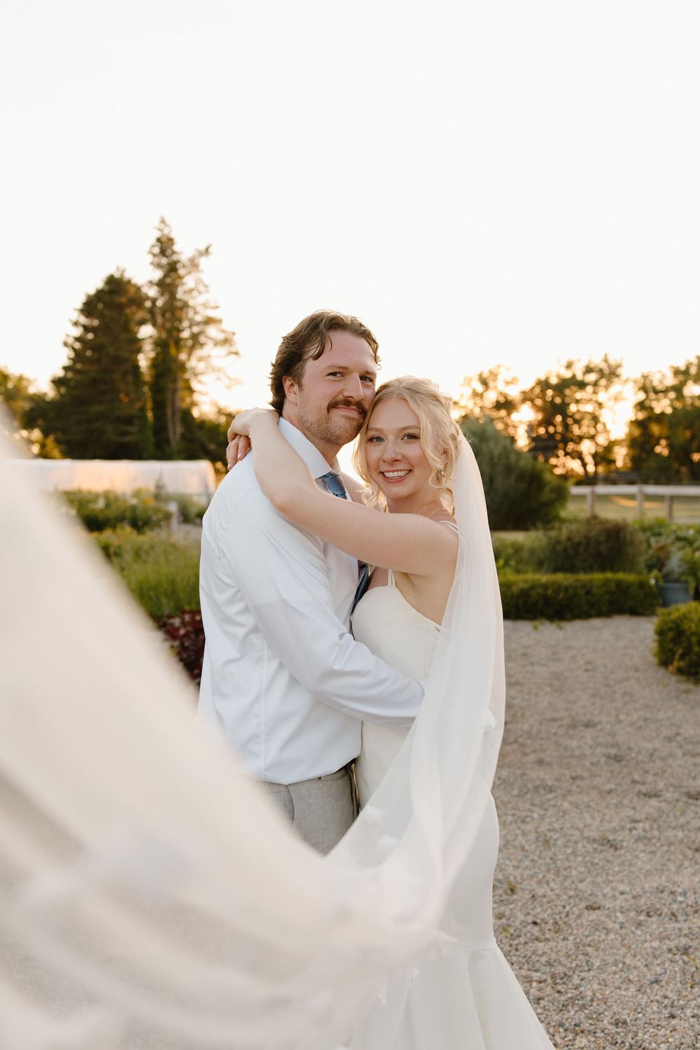 Couple embraces on a gravel path during their sunset wedding photoshoot.