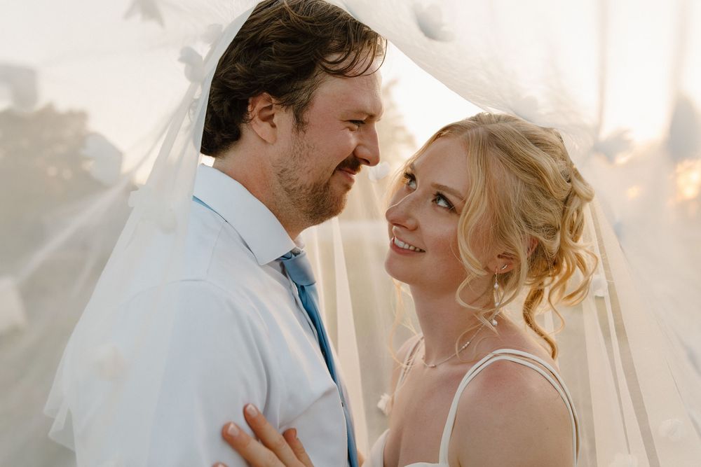 Romantic outdoor wedding portrait with soft lighting and flowing white fabric in the background.