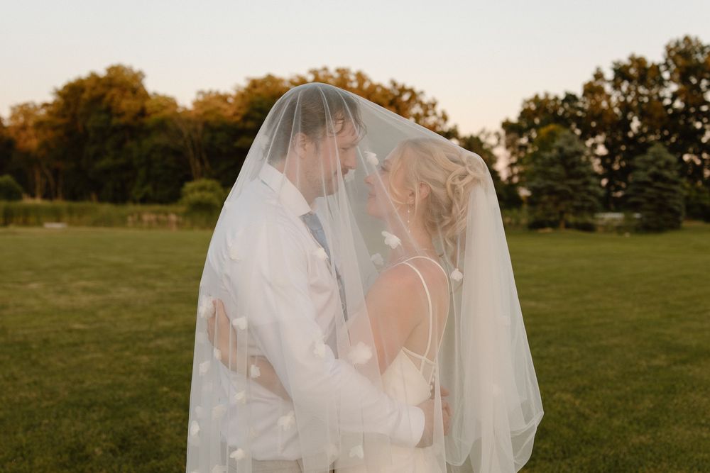 A romantic wedding moment captured during golden hour with the couple embracing under a flowing veil.