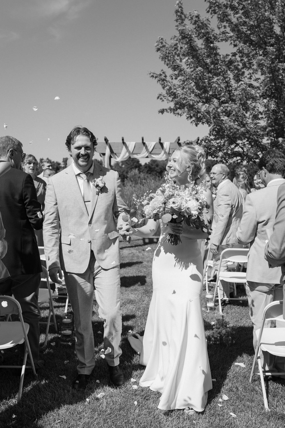 An outdoor wedding ceremony captures candid moments of guests and the bridal party on a sunny day near small white tents.