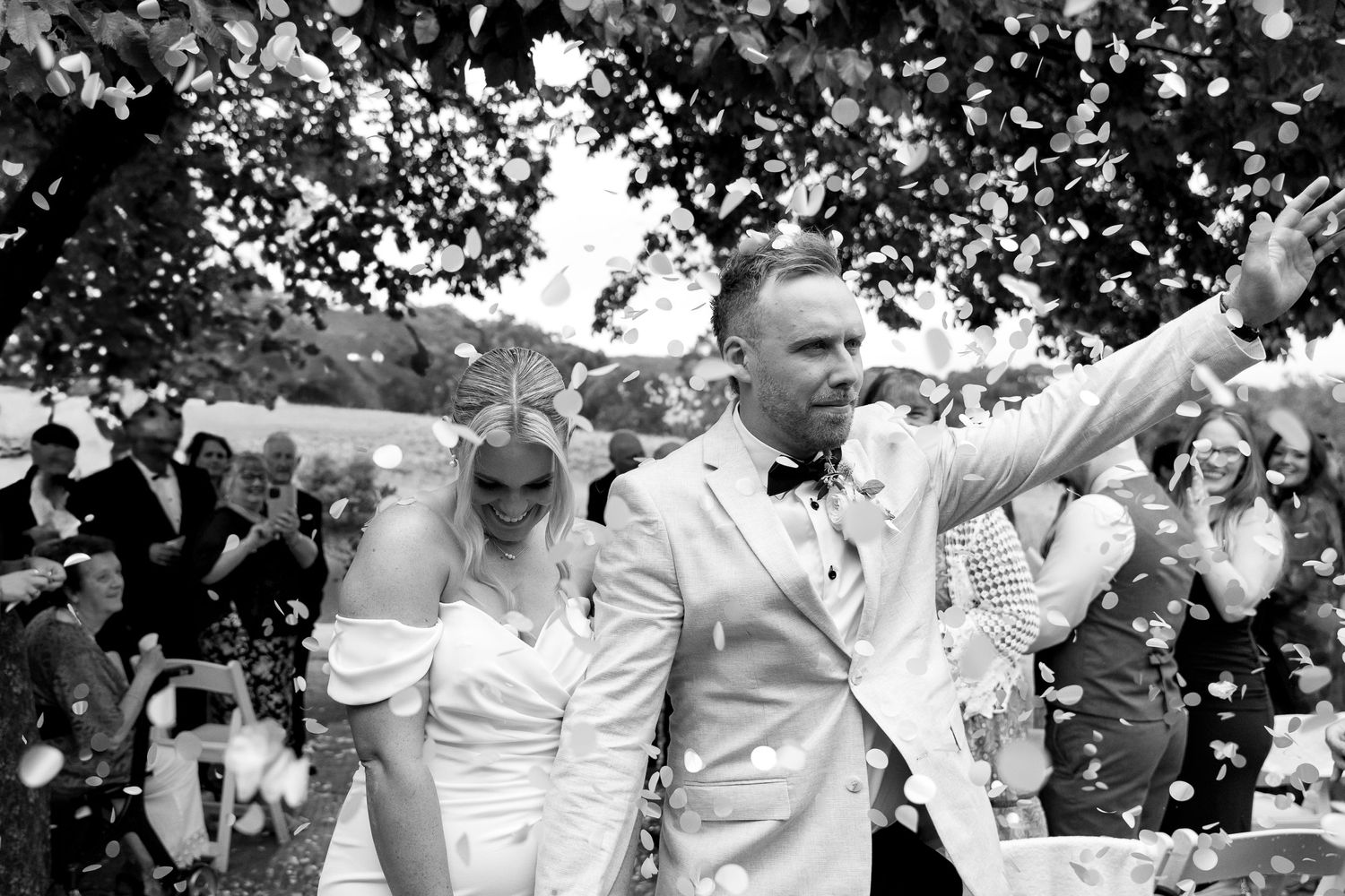 Wedding party in black and white throwing white flower petals outdoors.