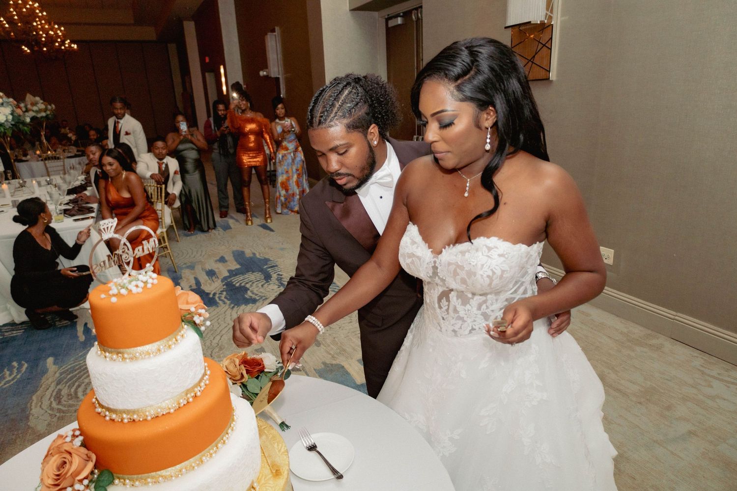 A bride and groom cut their elegant orange and white tiered wedding cake at their reception.