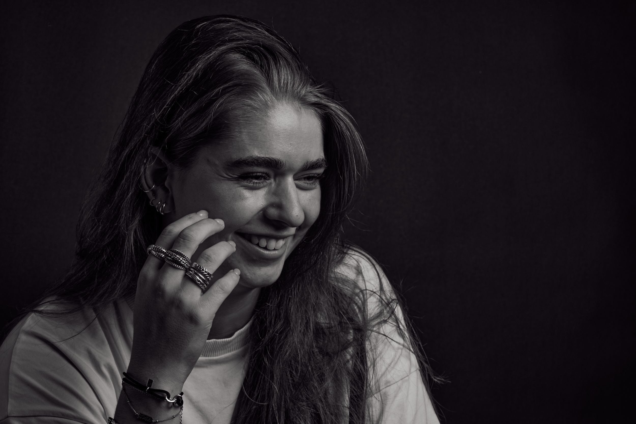 Zwart wit portret van een lachende jonge vrouw met ringen om haar vingers en een armband om