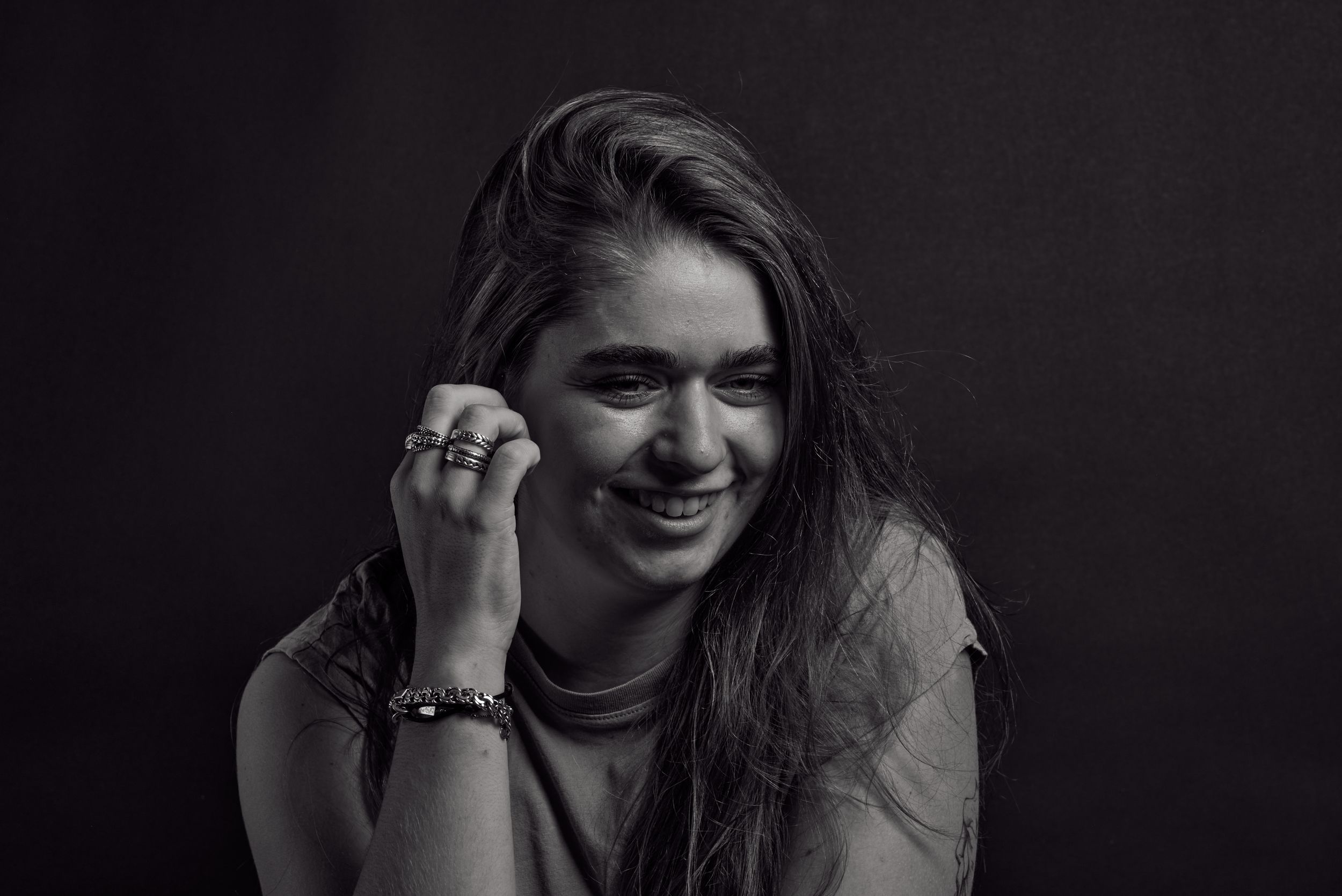 Zwart wit portret van een lachende jonge vrouw met ringen om haar vingers en een armband om