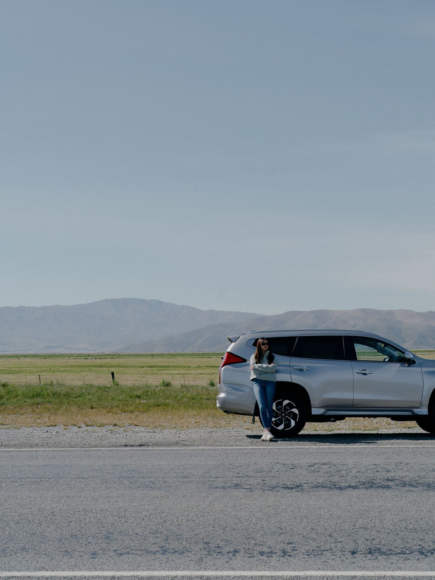 Silver SUV parked on road with mountains in background under clear sky.