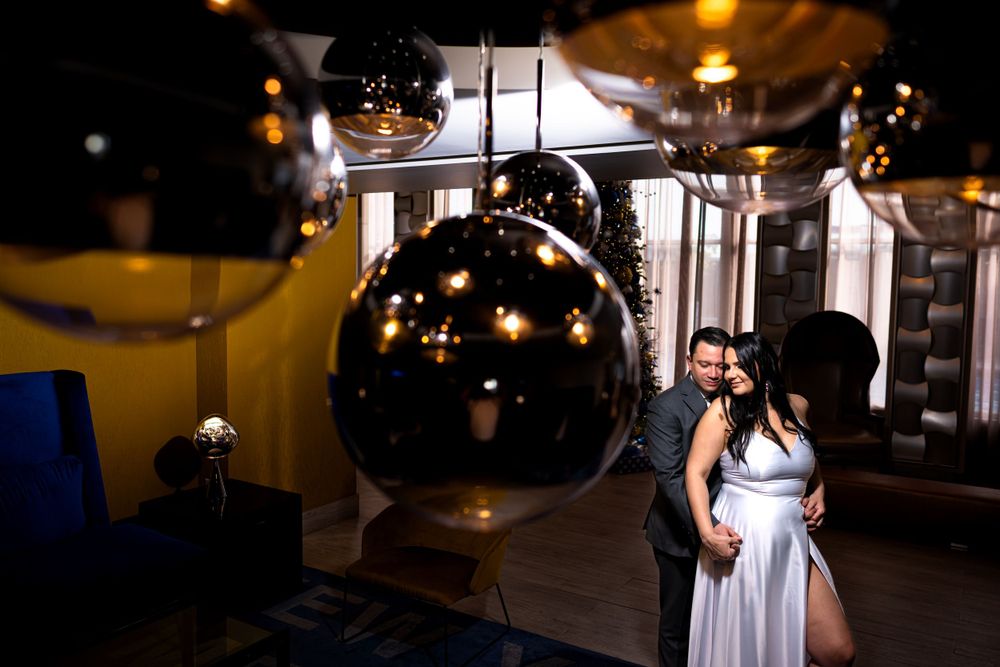 Woman in white dress poses beneath modern black spherical light fixtures.