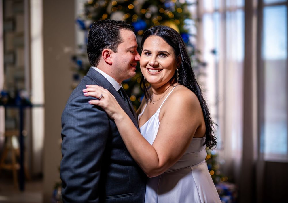 A couple shares an intimate moment in formal attire against a decorated interior background.