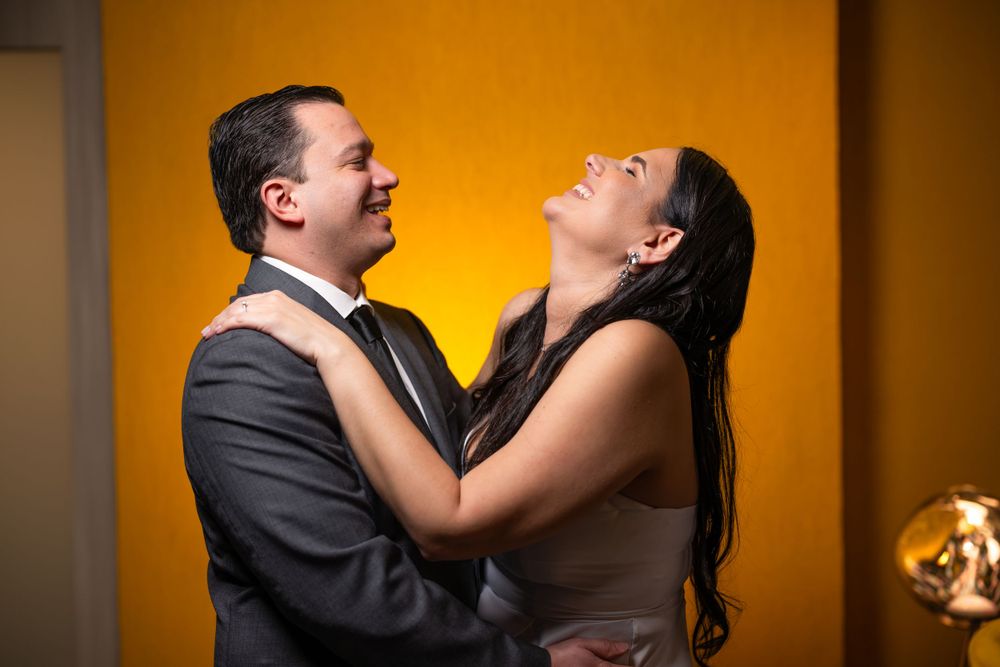 A couple shares a joyful embrace against a vibrant orange backdrop.