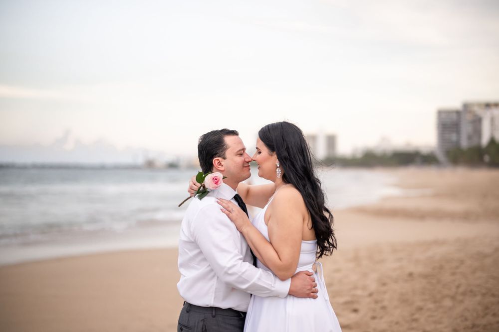A couple embraces on a sandy beach at sunset.