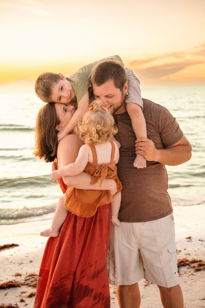 Family of four shares a joyful embrace and piggy back ride along the shoreline during a golden hour beach photography session in Florida.