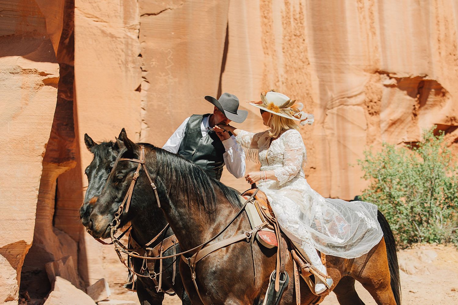 Couple in western attire sharing a romantic moment on horseback near red sandstone canyon walls.