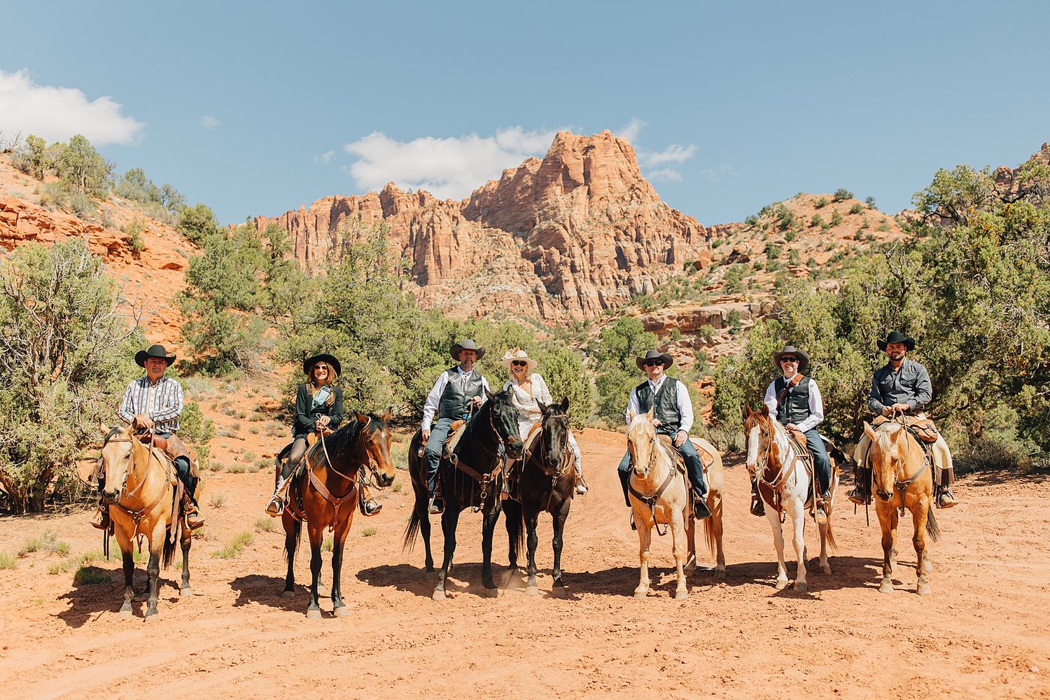 Six cowboys on horseback pose in a line against stunning red rock canyon formations in Sedona, Arizona.