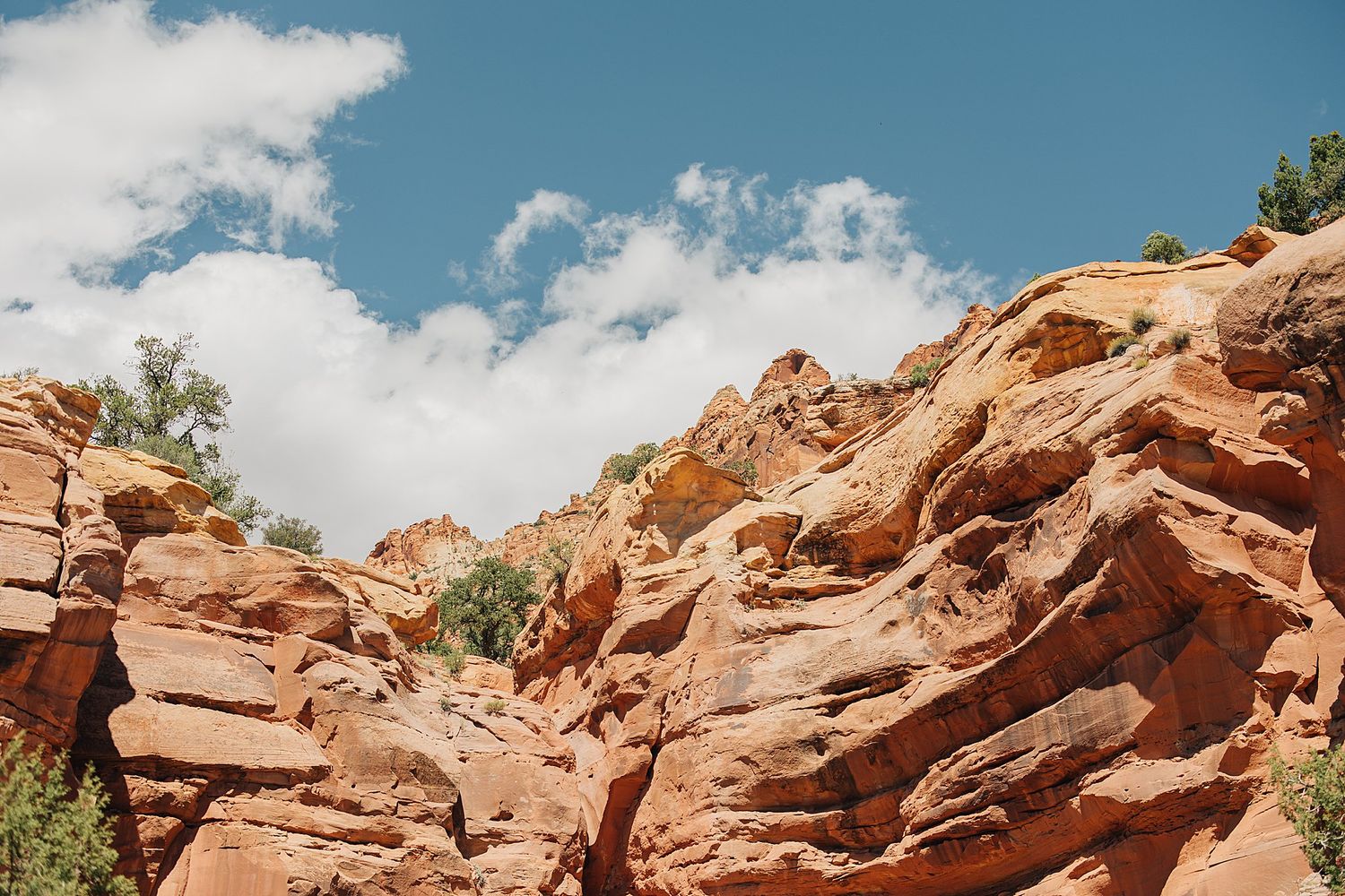 Dramatic red sandstone rock formations under a blue sky with white clouds in a desert canyon landscape.