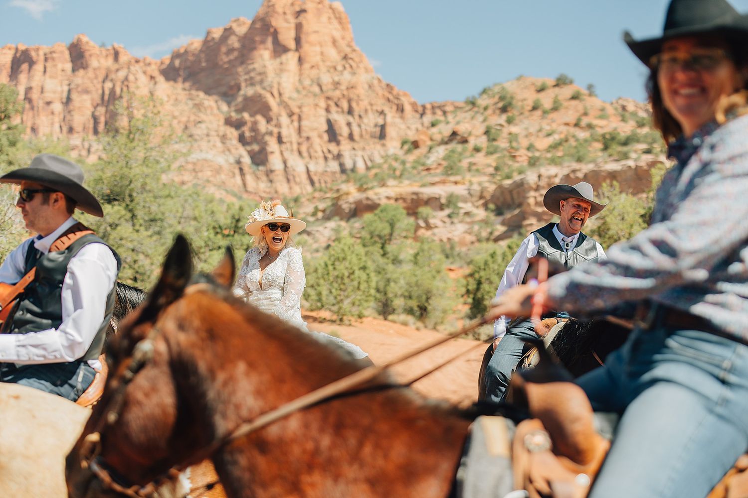 Group of people horseback riding through a scenic red rock canyon landscape on a sunny day.