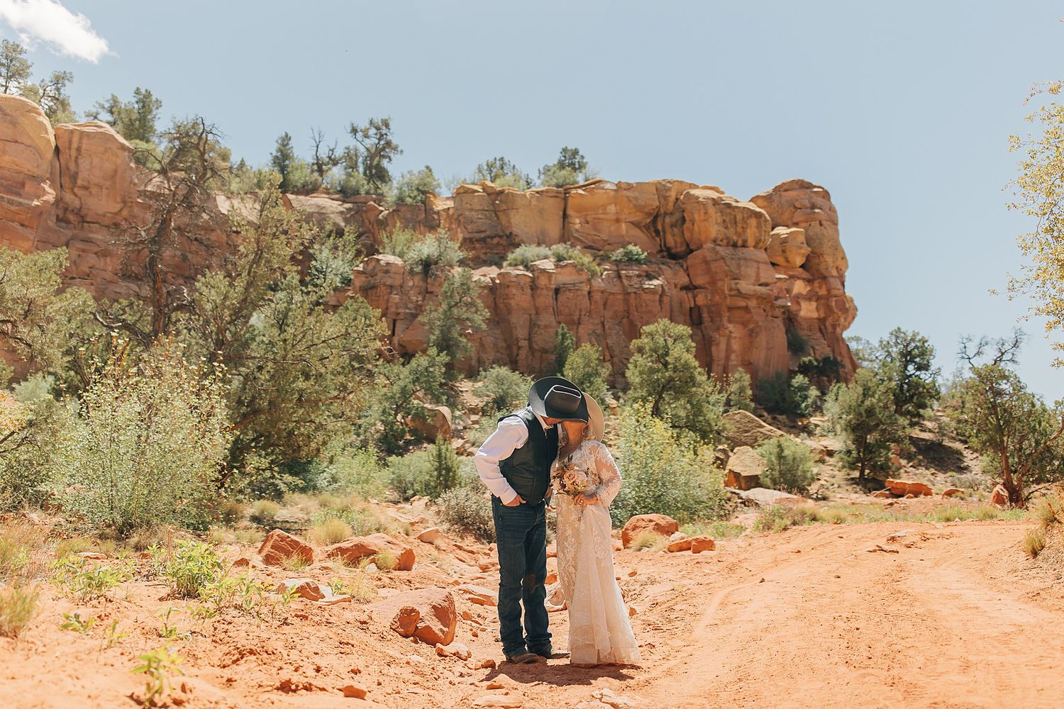 Bride and groom share a romantic kiss on a red dirt path surrounded by stunning red rock formations in Sedona, Arizona.