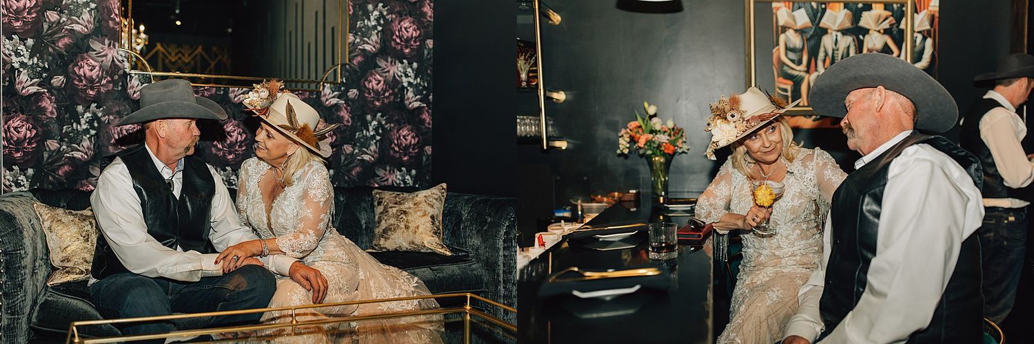 Elderly couple in vintage wedding attire share a romantic moment on ornate sofa in elegant dark floral venue.