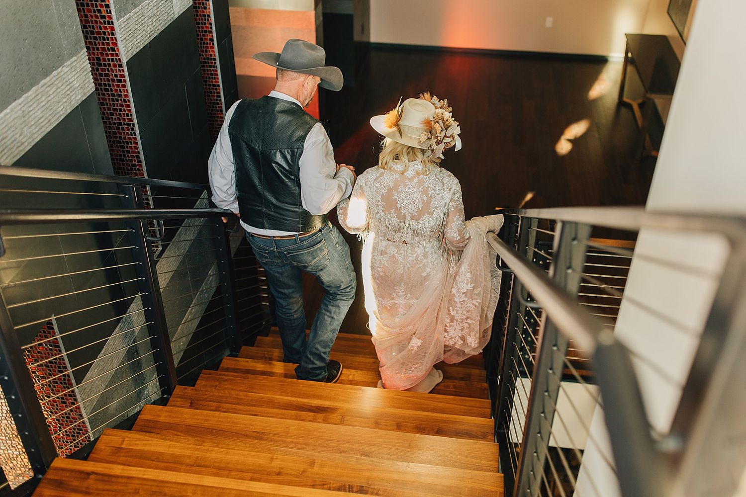 Bride and groom in western attire walking up wooden stairs at their rustic wedding venue.