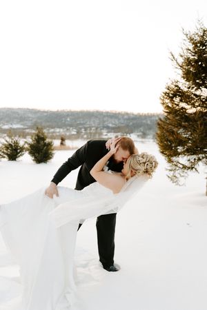 Groom dips bride for a romantic kiss in a snowy winter outdoor wedding setting.