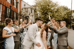 Bride and groom kiss while their wedding party celebrates with sparklers on a city sidewalk.