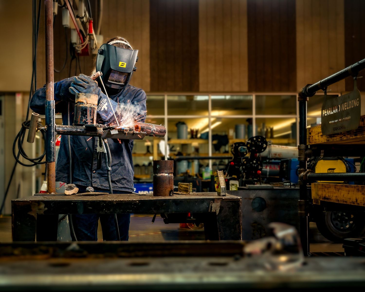 A welder in protective gear creates sparks while working on metal in a professional workshop.