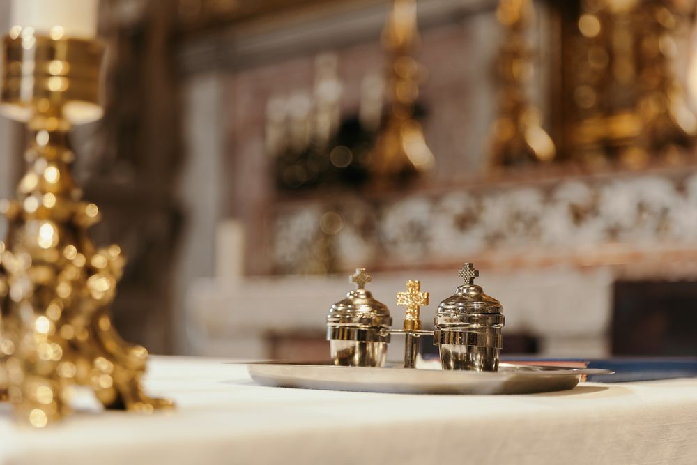 Gold and silver liturgical vessels on a white altar cloth in an ornate church setting.